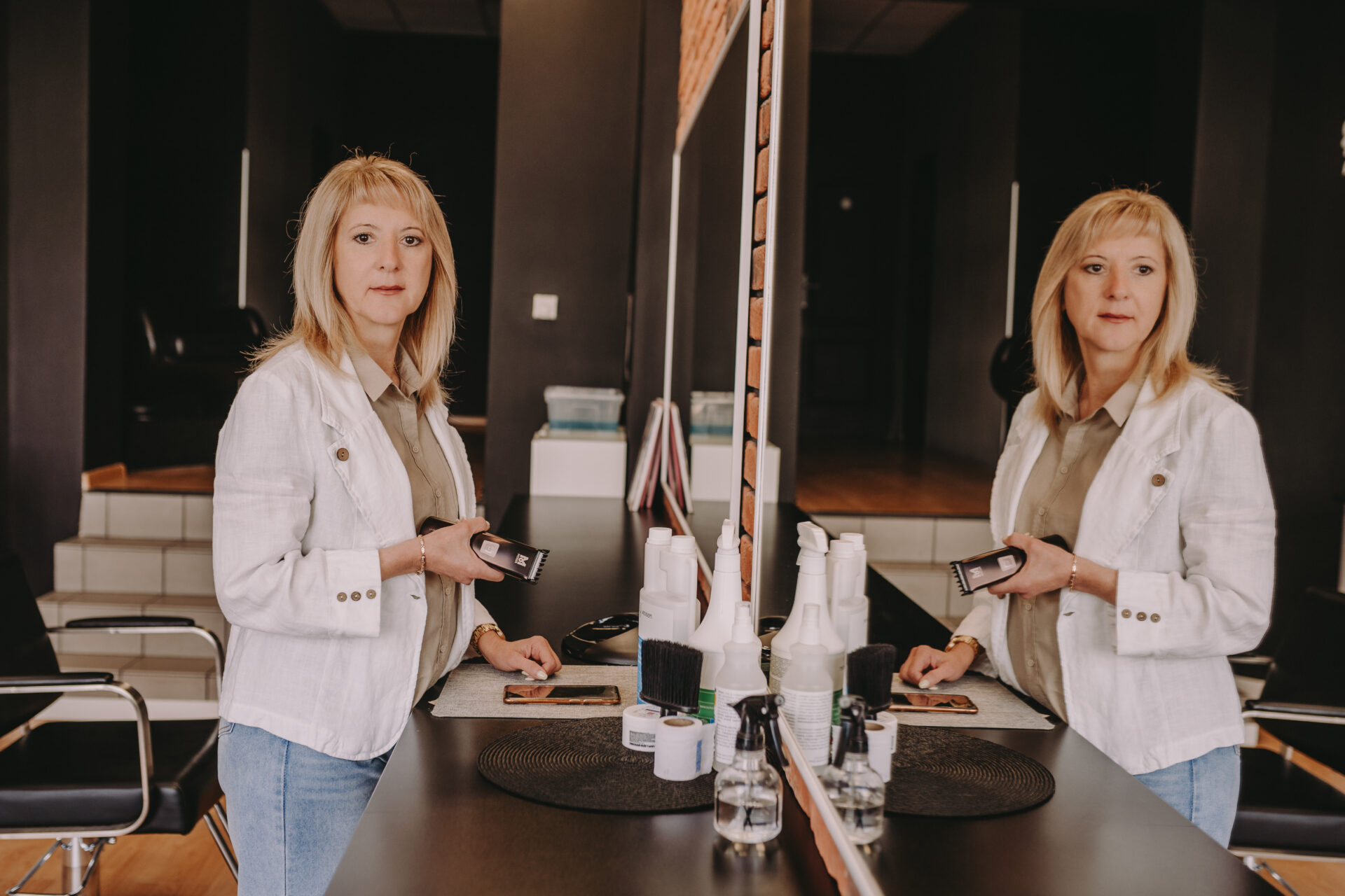 Fryzjerka Olena Pavlenko w salonie fryzjerskim Ameliia w Szczecinie trzyma telefon i golarkę do włosów